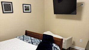 Un dormitorio con una cama, un televisor montado en la pared y dos citas enmarcadas.