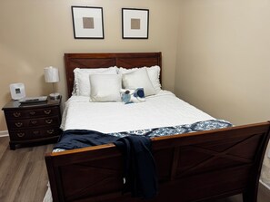A neatly made bed with a patterned bedspread, a wooden headboard, and a nightstand with a lamp and a phone. - Cozy 1-bedroom studio, Near Daffin Park, 10 min away from Downtown, on bus route (Savannah)