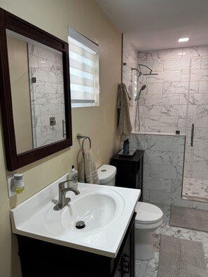 A bathroom with a white sink, a toilet, a shower with a glass door, and a mirror with a wooden frame. - Cozy 1-bedroom studio, Near Daffin Park, 10 min away from Downtown, on bus route (Savannah)
