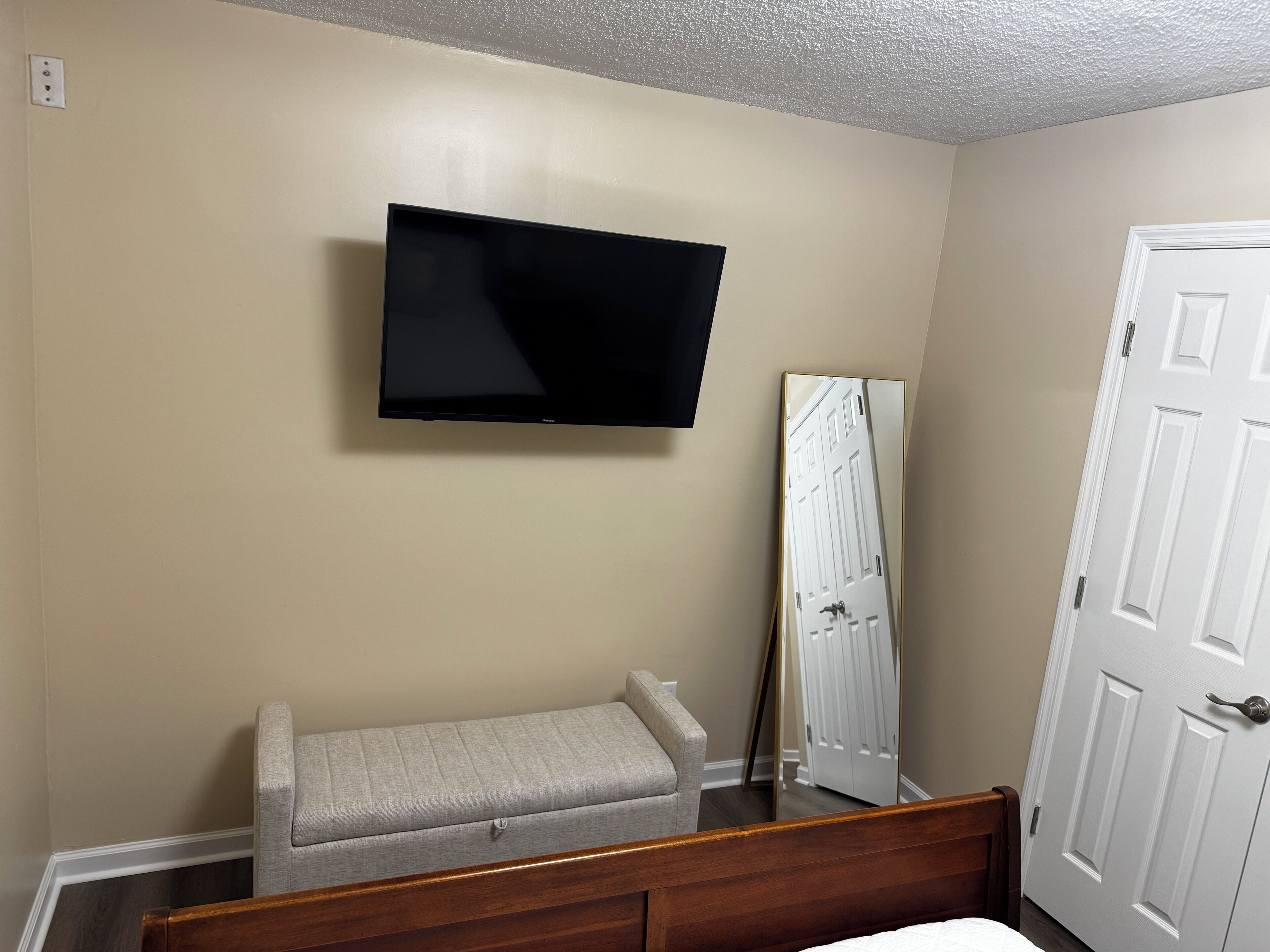 A bedroom with a bed, a bedside table, a television mounted on the wall, and a door.