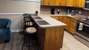 Una cocina con armarios de madera, un taburete de bar, una cafetera y un microondas.