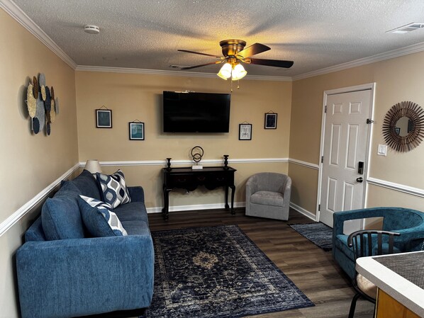 A living room with a sofa, armchair, and a small table with a TV above. - Cozy 1-bedroom studio, Near Daffin Park, 10 min away from Downtown, on bus route (Savannah)