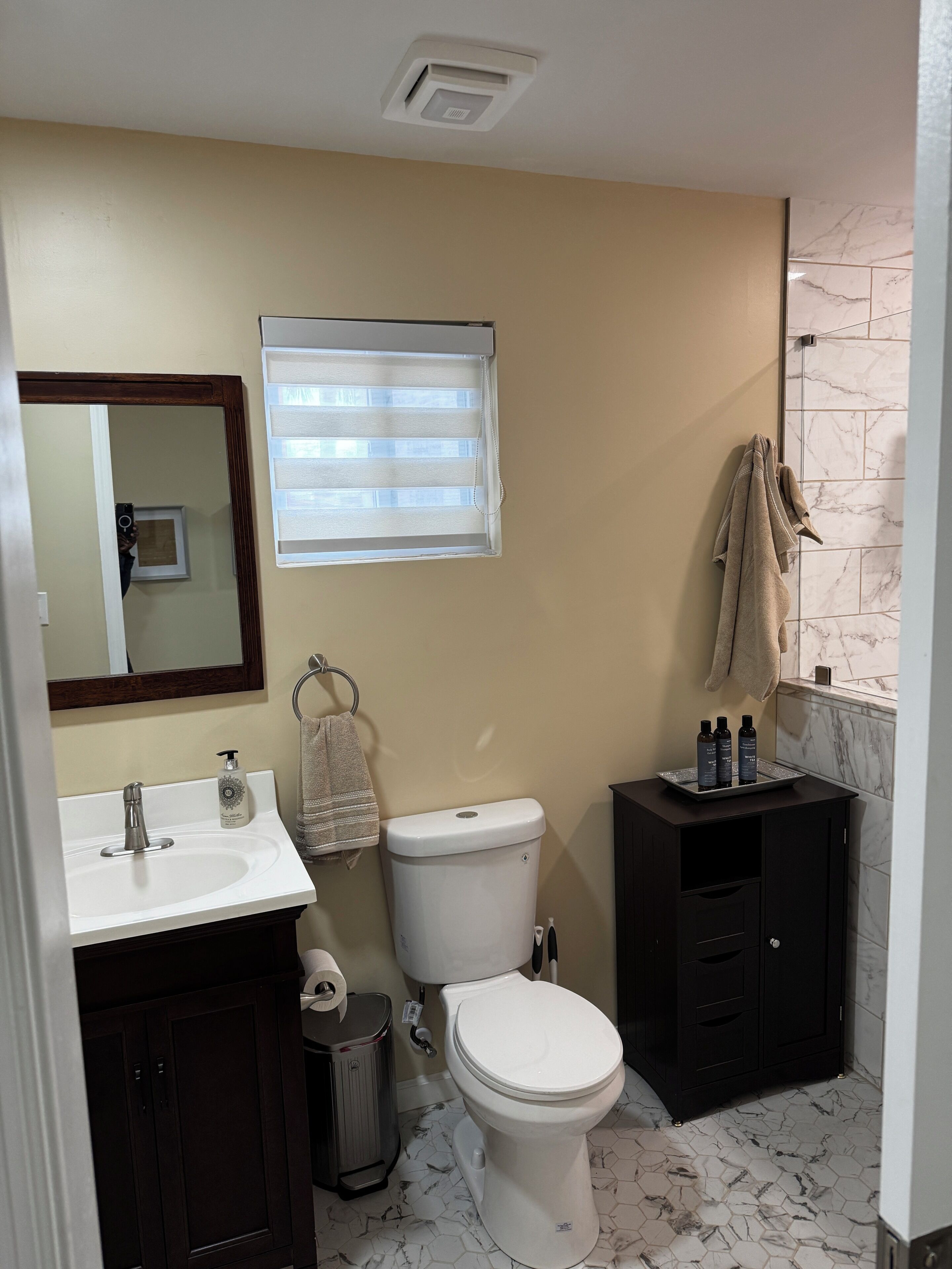 A bathroom with a toilet, sink, vanity, and a window with blinds.