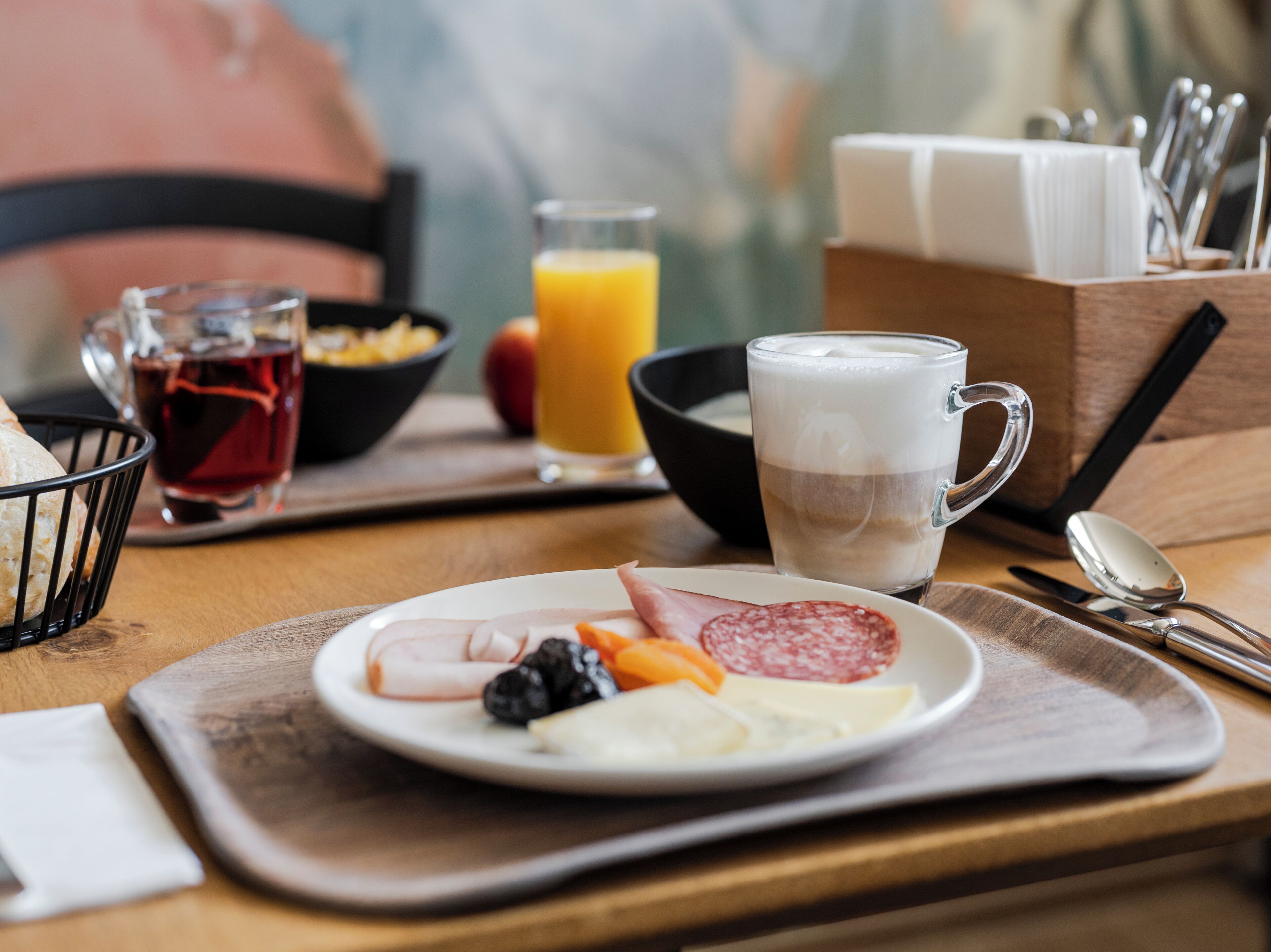 Bandeja de desayuno con jamón, queso y fruta, un vaso de zumo de naranja y una taza de café.