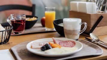 Bandeja de desayuno con jamón, queso y fruta, un vaso de zumo de naranja y una taza de café.