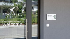 Une entrée d’hôtel moderne avec une porte en verre, un panneau d’accueil et une signalétique indiquant l’entrée.