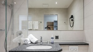 Une salle de bain moderne avec une douche à l’italienne en verre, un lavabo blanc et un grand miroir.