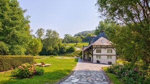 Ein traditionelles Haus mit einem steinernen Weg, der zu einer Rasenfläche mit einer Bank führt.
