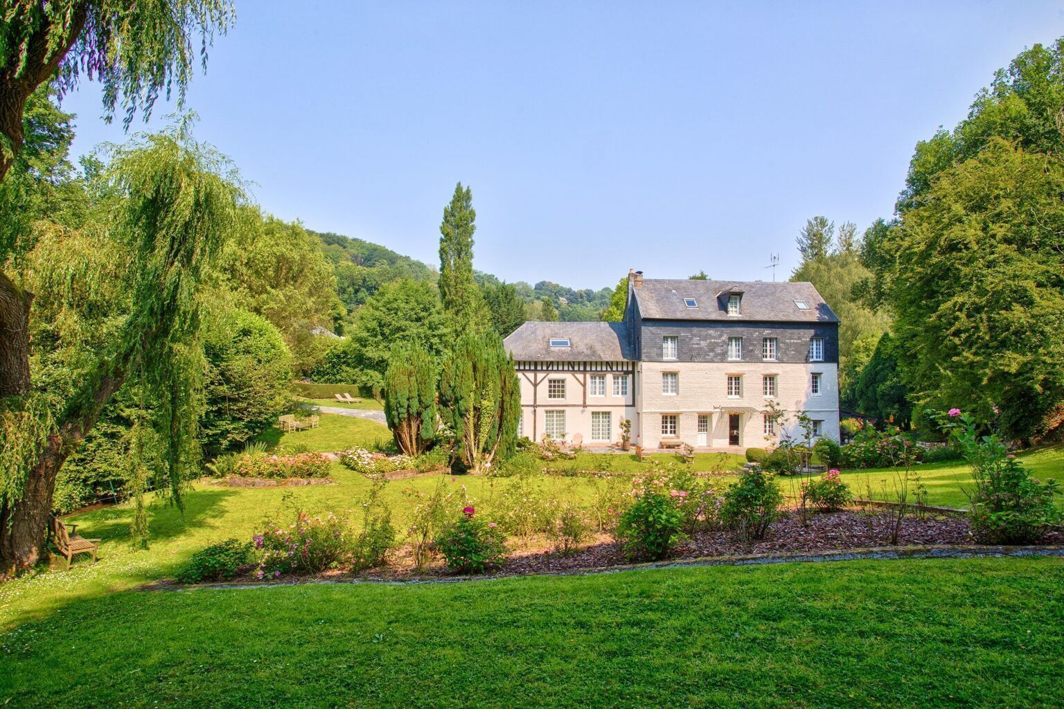 A large, two-story house with a garden in front, surrounded by trees and hills.