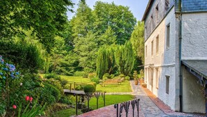 Ein Garten mit einem Kiesweg, der zu einem Gebäude mit weißer Fassade und Ziegelbasis führt.