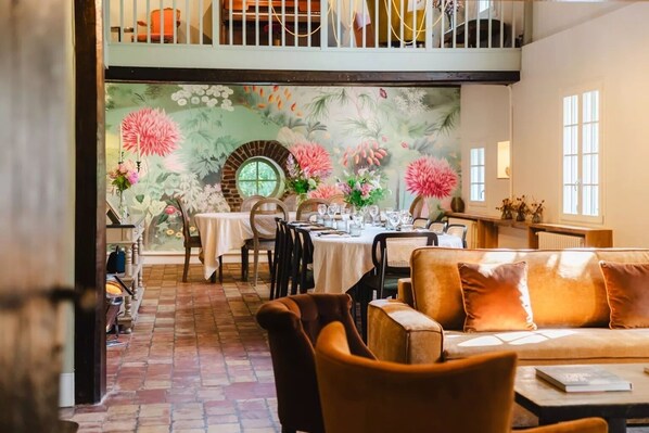 Un espace repas avec des tables dressées pour le repas, un canapé et un escalier menant à un niveau supérieur.