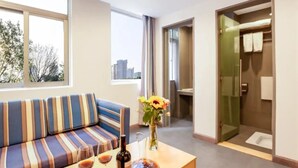 A hotel room with a sofa, a table with a bottle and glasses, a vase with flowers, and a view of the city through large windows. - SHENZHEN CHENGBANG LIGHT LUXURY APARTMENTS (Shenzhen)