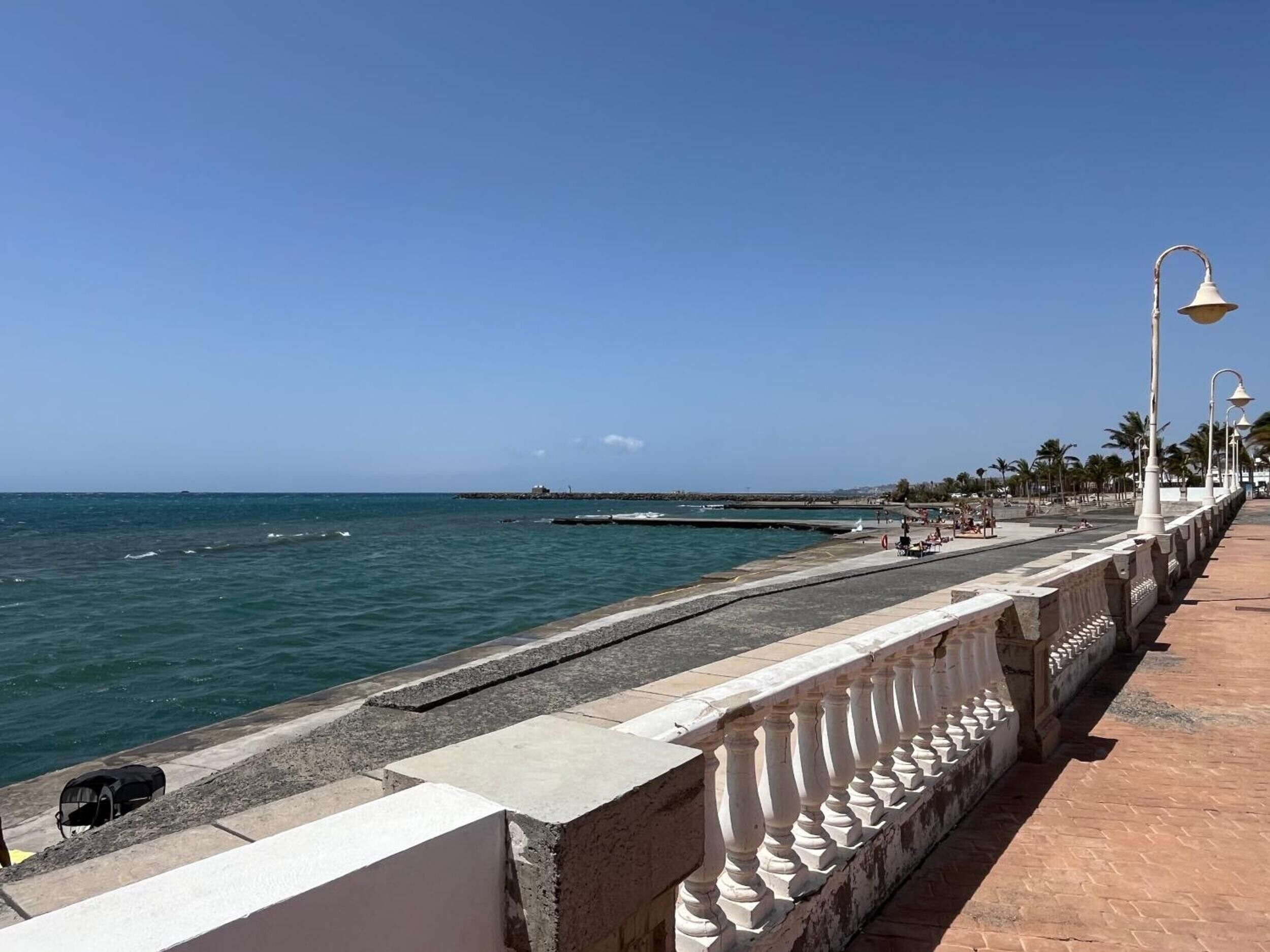 Eine Küstenpromenade mit Steinbalustrade, blauem Himmel und ruhiger See.