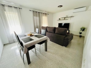 Uma sala de estar com sofá, televisão e área de jantar com mesa e cadeiras.
