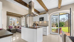Une cuisine moderne dotée d’un îlot central, de meubles blancs et d’une grande porte-fenêtre coulissante donnant sur un patio extérieur.
