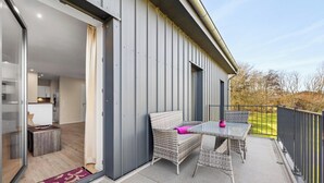 Un balcón al aire libre con muebles de mimbre, una mesa de vidrio y un cojín rosa.
