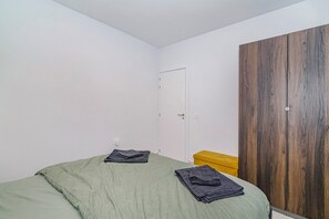 Ein Einzelbett mit grüner Bettdecke, ein Holzschrank und eine gelbe Bank.