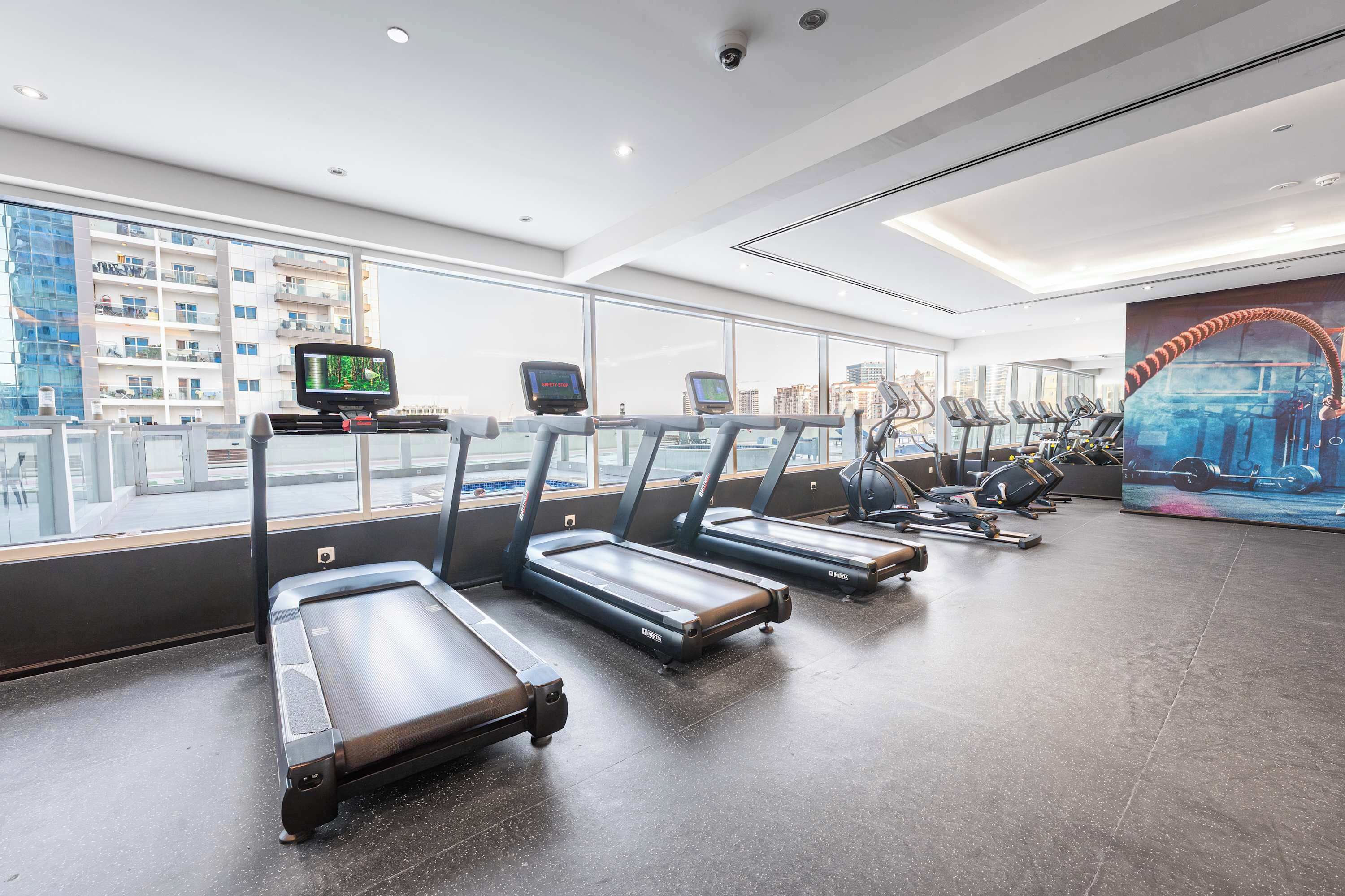 Ein Fitnessstudio mit Laufbändern, Ergometer und einem großen Fenster mit Blick auf die Stadt.