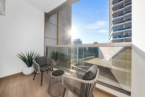 A balcony with wicker furniture, a potted plant, and a view of a high-rise building. - StayShort - Cozy Studio in Sports City that Sleeps 3 (Sports City)