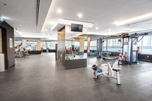 A modern gym with various exercise equipment, a reception desk, and large windows offering views of the city. - StayShort - Cozy Studio in Sports City that Sleeps 3 (Sports City)