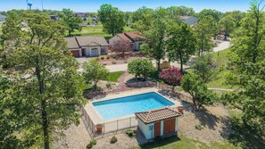 A residential area with a swimming pool, a small building, and surrounding trees. - Sunset Ridge Private Patio (Lake Ozark)