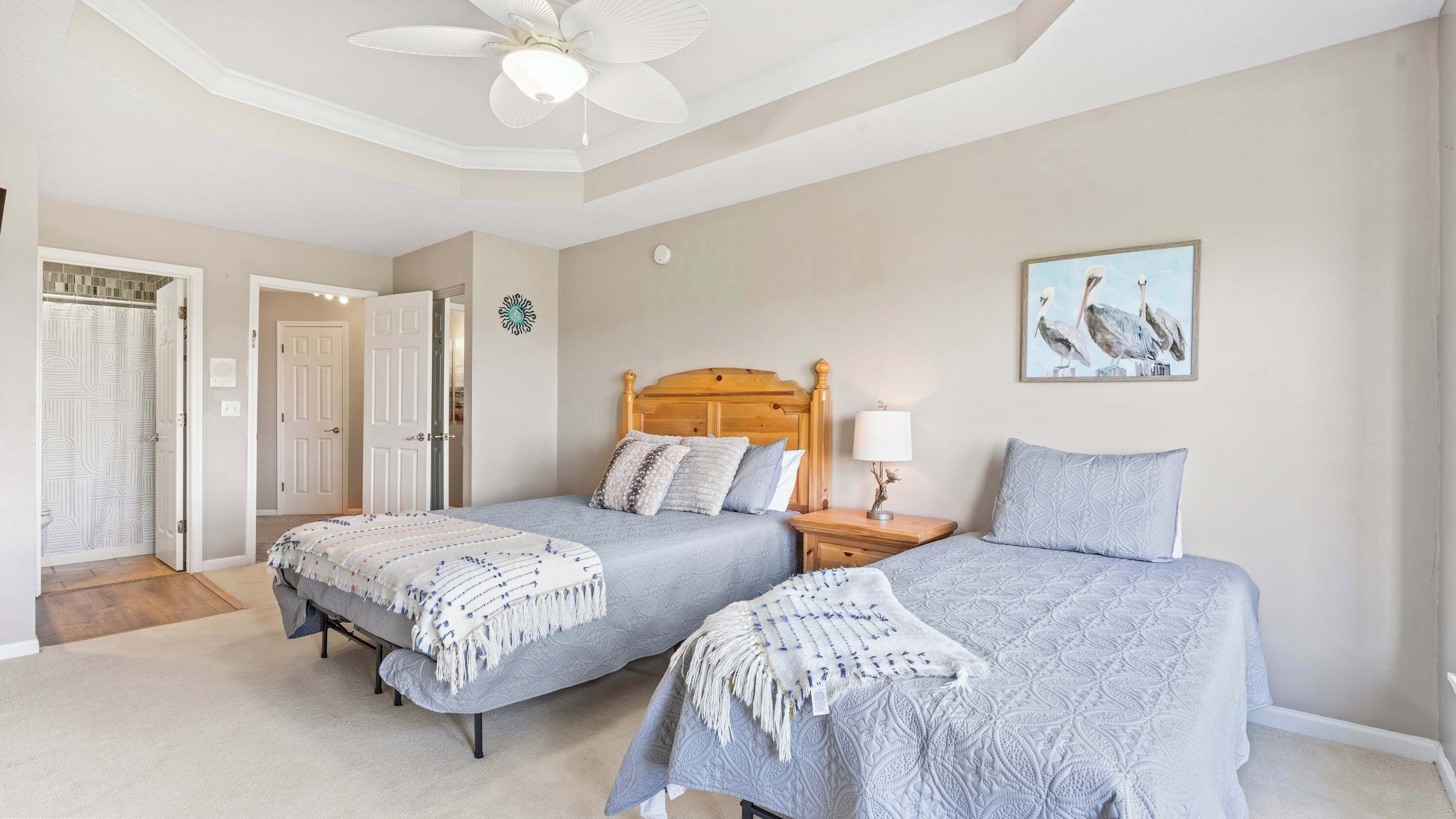 A bedroom with two beds, a ceiling fan, a nightstand, a lamp, and a framed picture on the wall.