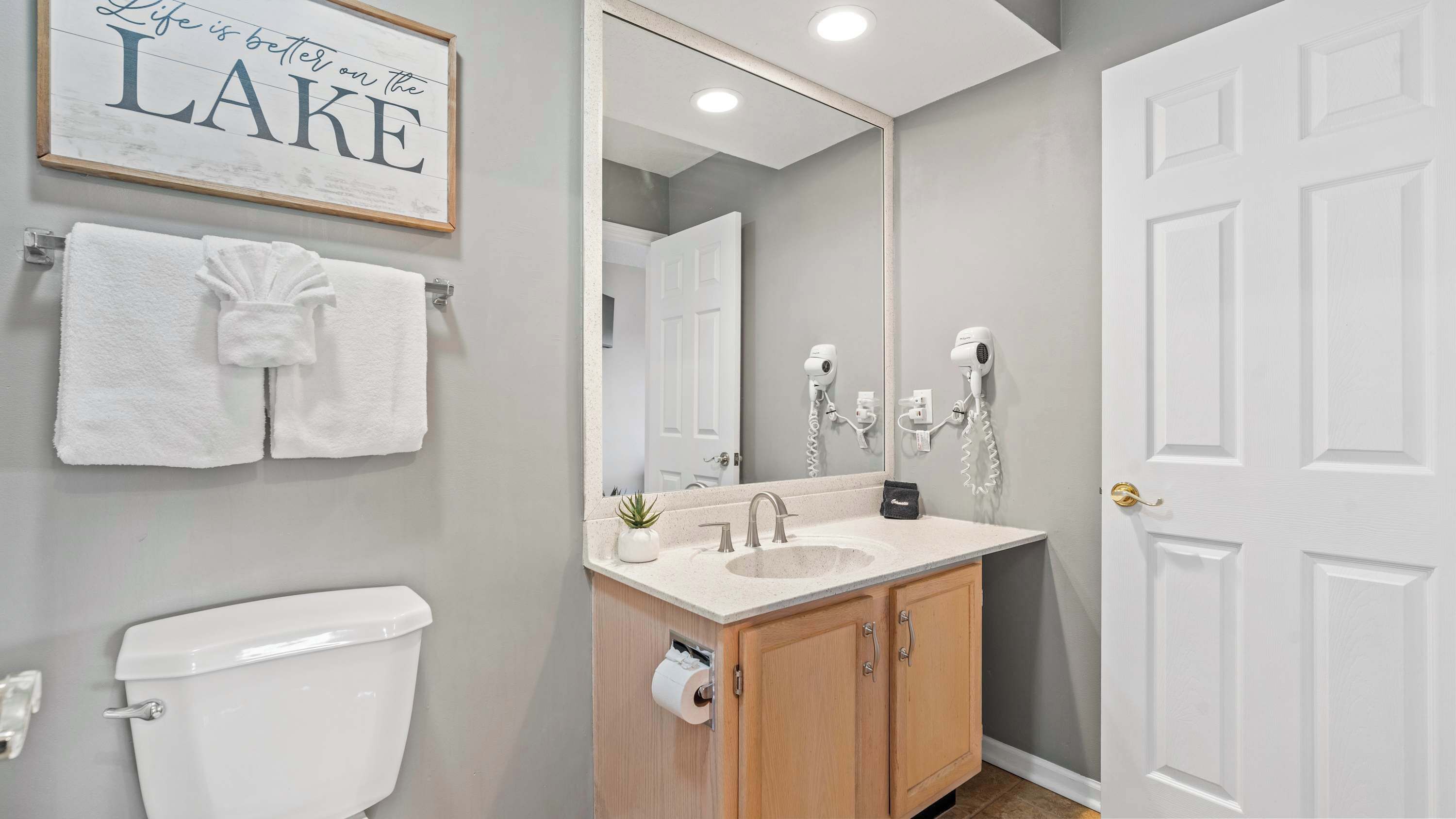 A bathroom with a toilet, sink, mirror, towel rack, and a framed sign on the wall.