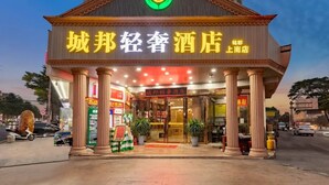 Ein Hotel mit einer markanten Fassade, einem grünen Logo über dem Namen und einem Schild, das den Standort im Gebiet Shandong anzeigt.