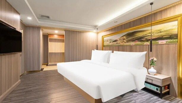 Ein modernes Hotelzimmer mit einem großen Bett, einem Flachbildfernseher, einem Gemälde an der Wand und einem Nachttisch mit Blumen.