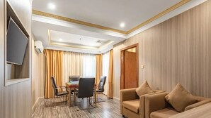 Ein Hotelzimmer mit Holzboden, einer Couch, einem an der Wand befestigten Fernseher und einem Essbereich mit Tisch und Stühlen.