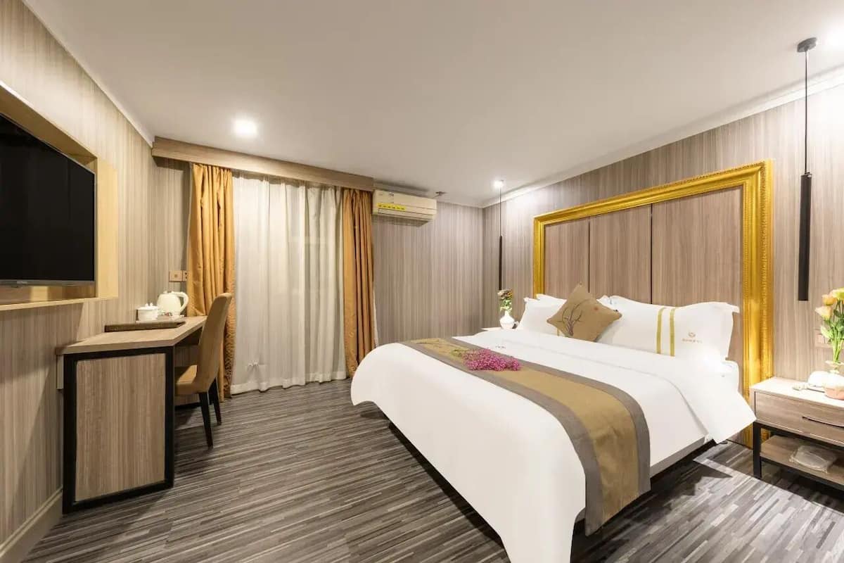 Una habitación de hotel con cama, escritorio, silla, televisor y mesita de noche.