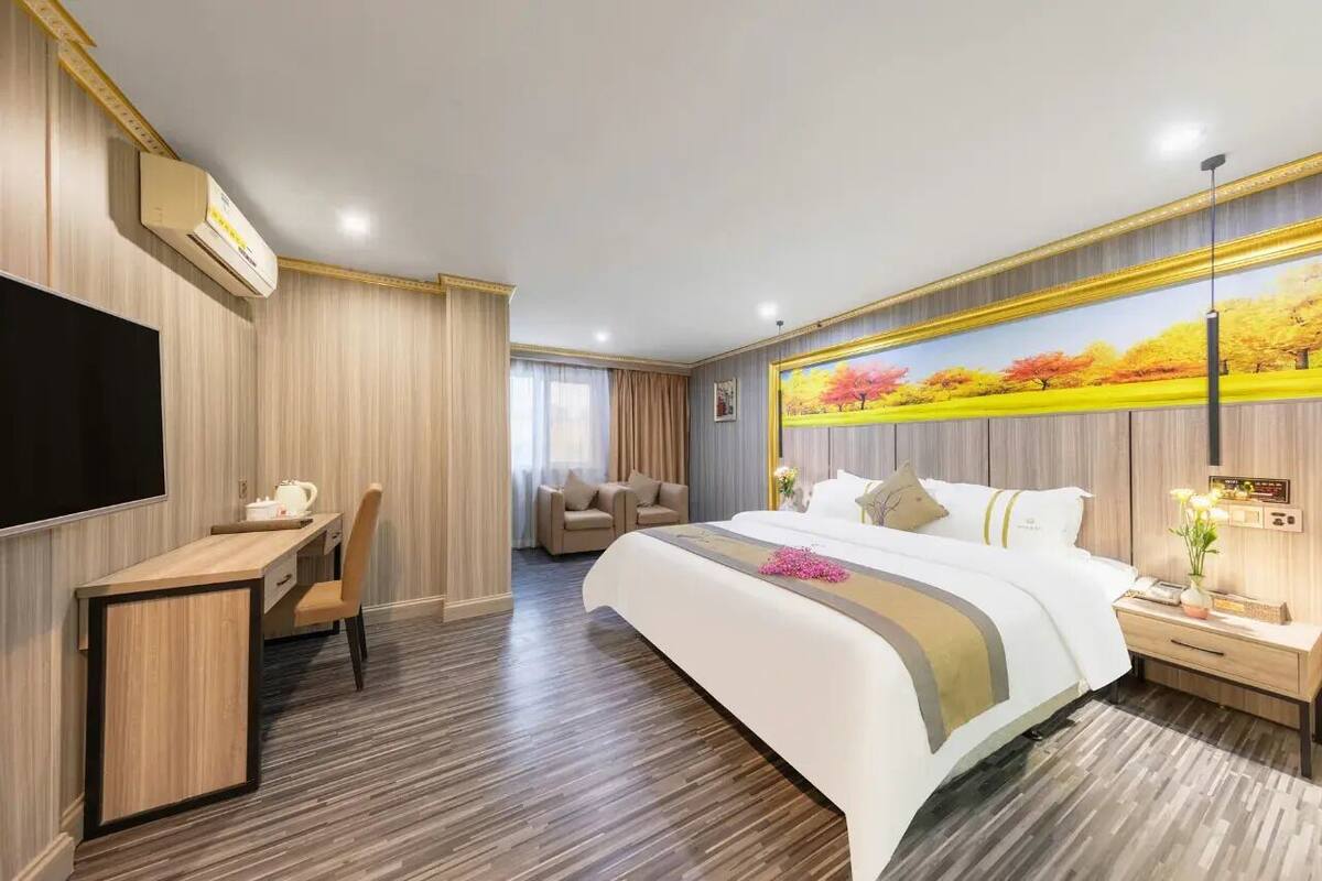Una habitación de hotel con cama, escritorio, silla, televisor y un cuadro en la pared.