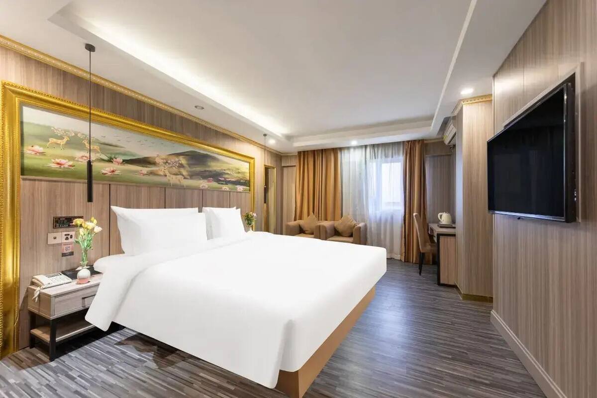 Habitación de hotel con una cama grande, un escritorio, una silla, un televisor y un cuadro en la pared.