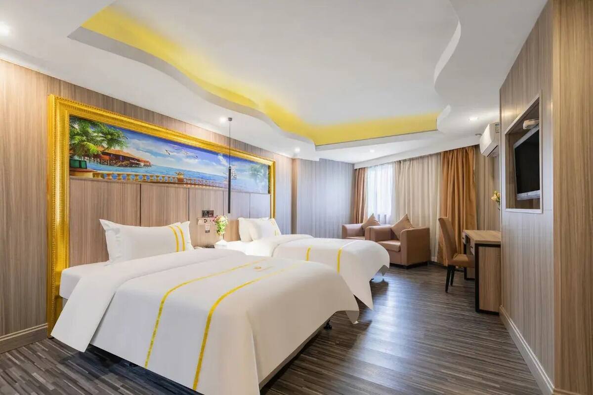 Habitación de hotel con dos camas, un escritorio, una silla, un televisor y un cuadro en la pared.