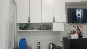 Cozinha compacta com armários brancos, pia de aço inoxidável, fogão e geladeira preta.