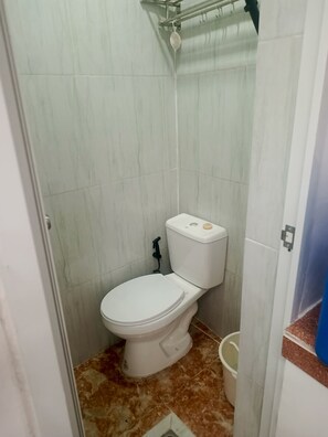 Une petite salle de bain avec des toilettes, une tringle pour le rideau de douche et un seau.