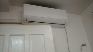 Unidade de ar condicionado branca fixada na parede acima de uma porta branca.