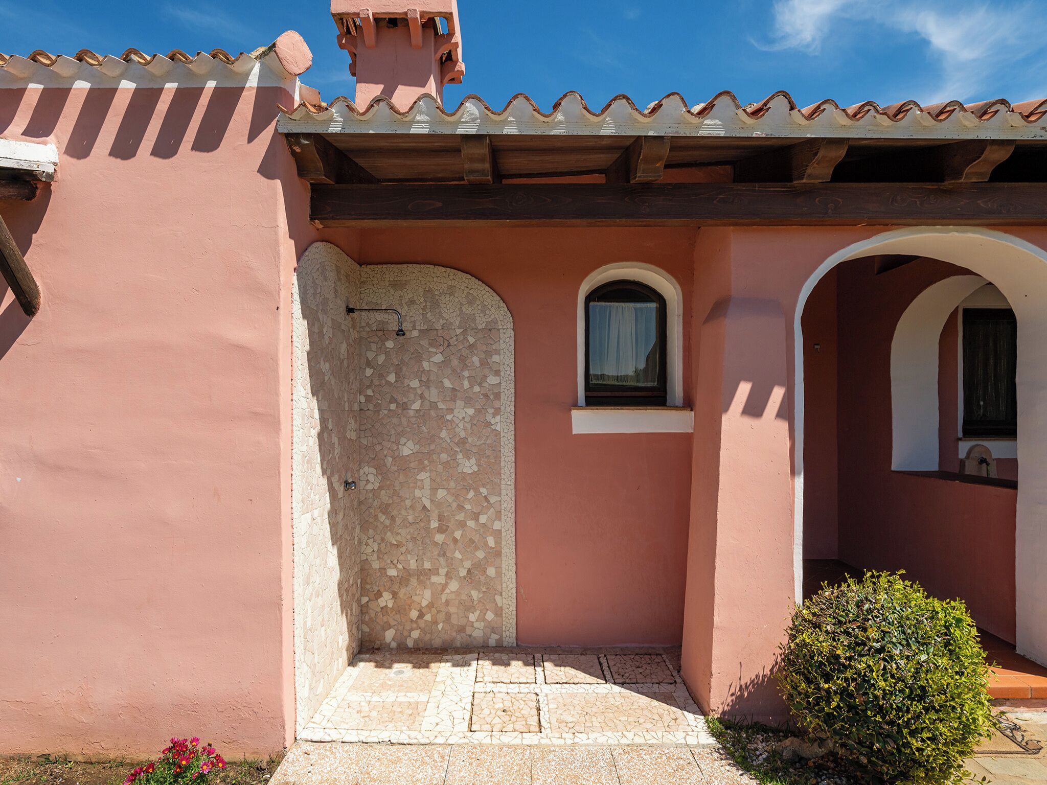 A building with a tiled roof, a door with a window, and a small garden area.