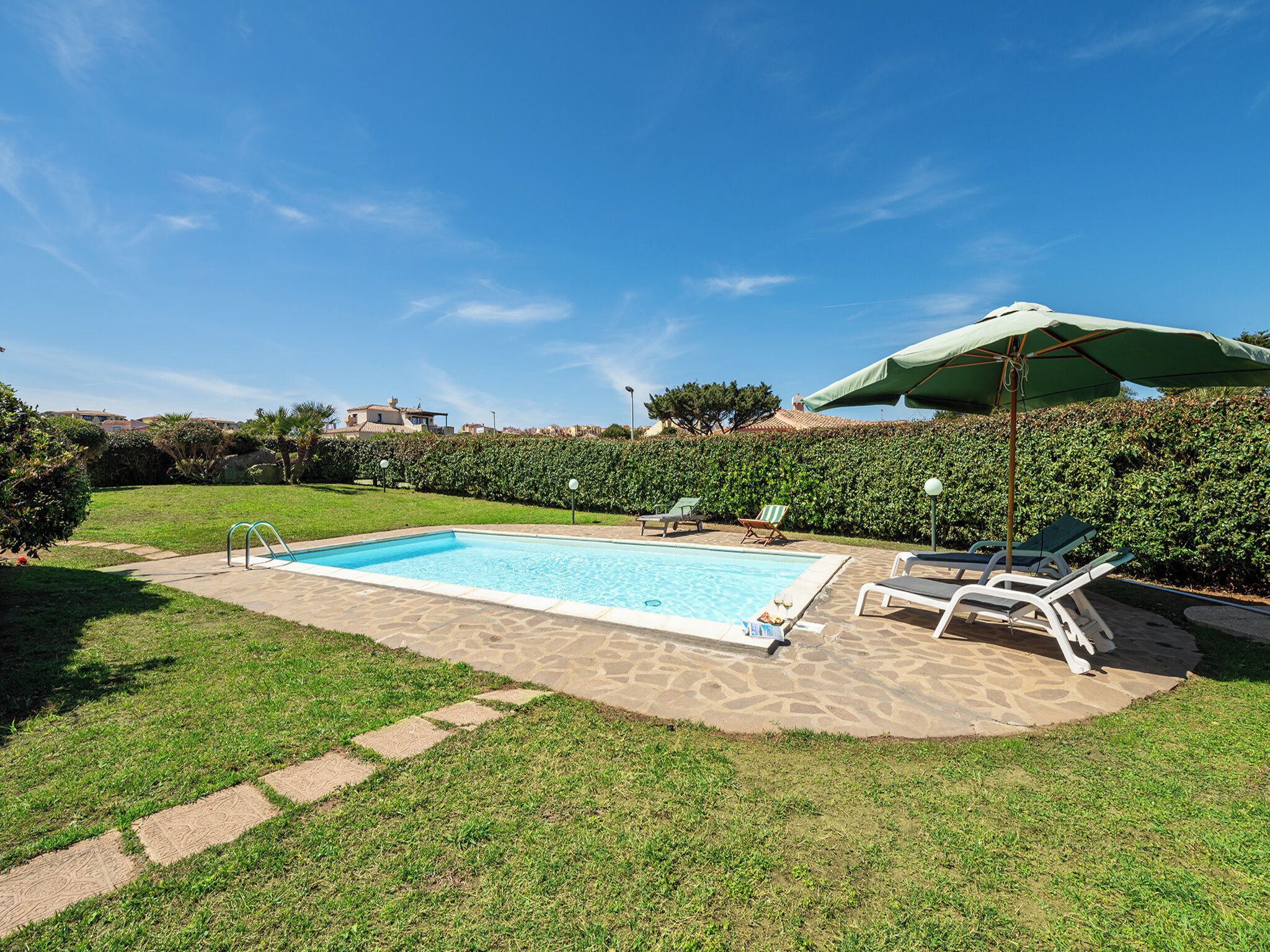 Una piscina con solárium de piedra, rodeada de césped y setos.