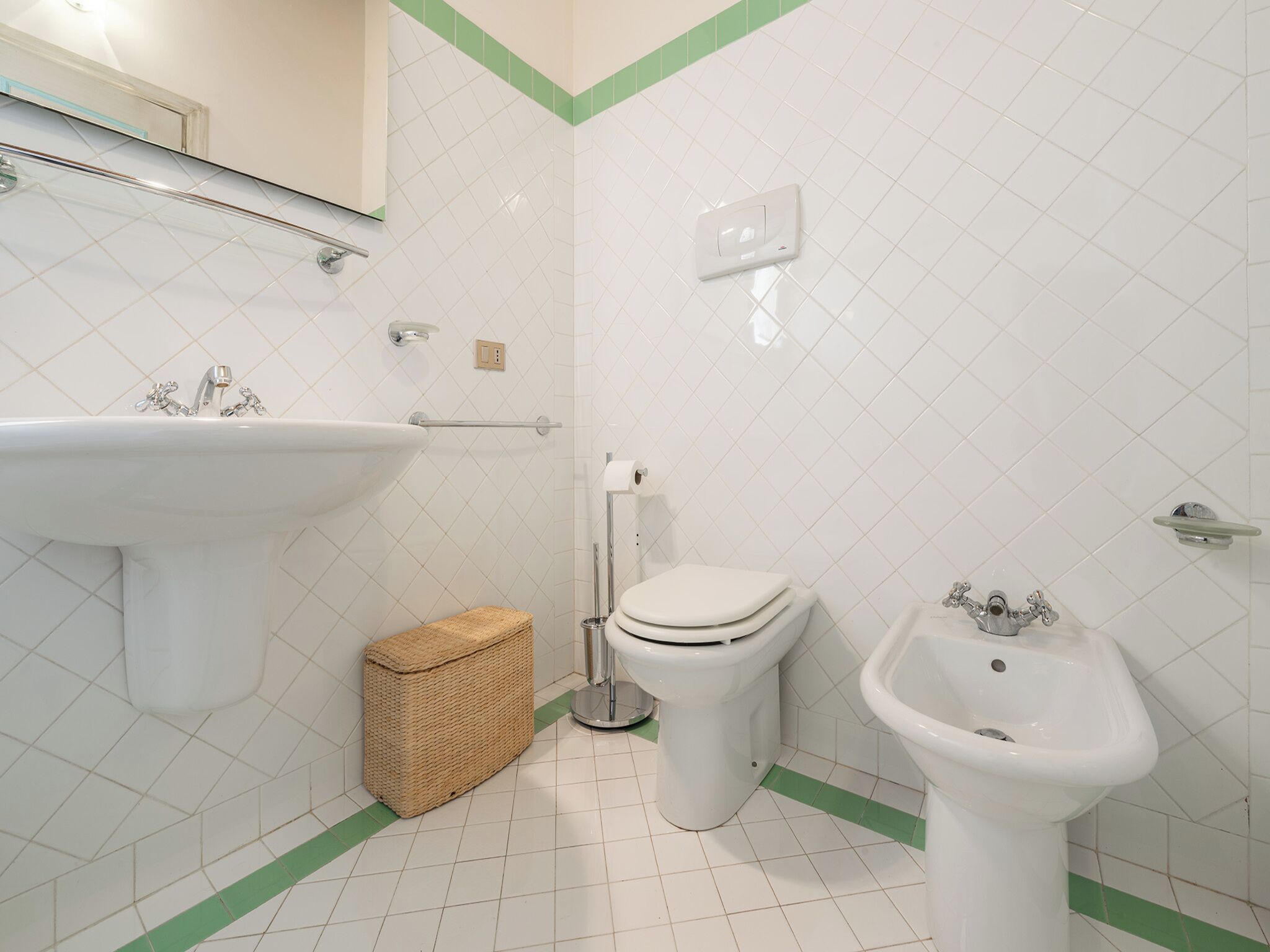 A bathroom with a sink, toilet, bidet, and a small wicker basket.