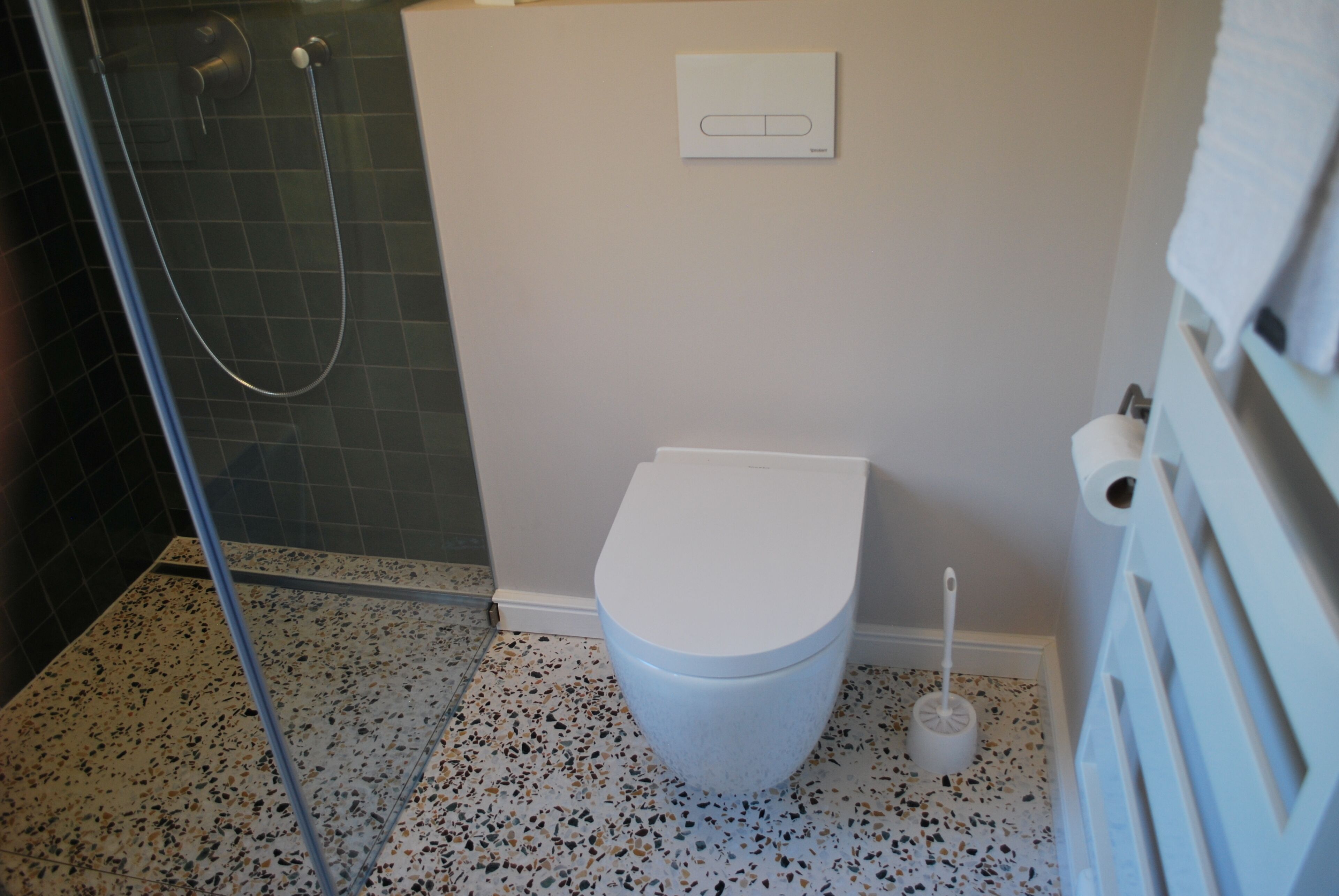 Et badeværelse med et hvidt toilet, et bruseområde og en håndtørrer.