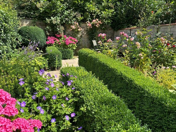 A garden with neatly trimmed hedges, flowering plants, and a stone wall. - The Friesen Cottage in Friedrichstadt with garden and terrace (Friedrichstadt)