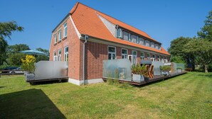 En tvåvåningsbyggnad i tegel med ett rött tegeltak, ett takförsett utomhusområde med stolar och bord, och en klarblå himmel.