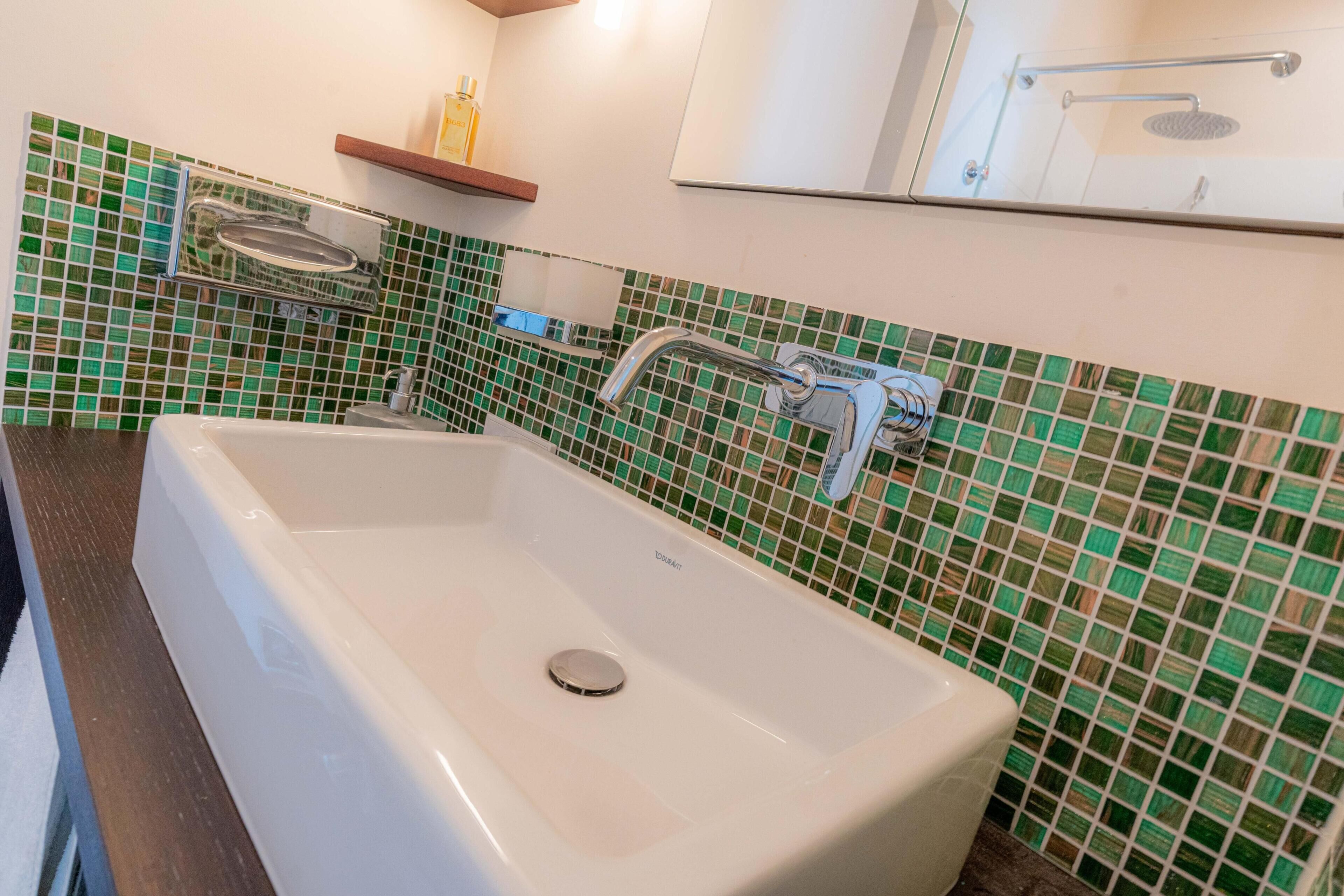 Une salle de bain avec un lavabo rectangulaire, un miroir et un espace douche.