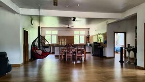 A spacious living area with a dining table, chairs, a hanging chair, and a kitchen in the background.
