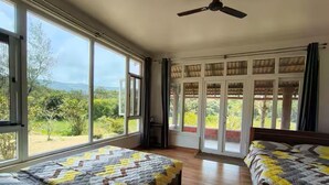 A room with two beds, large windows, and a ceiling fan.