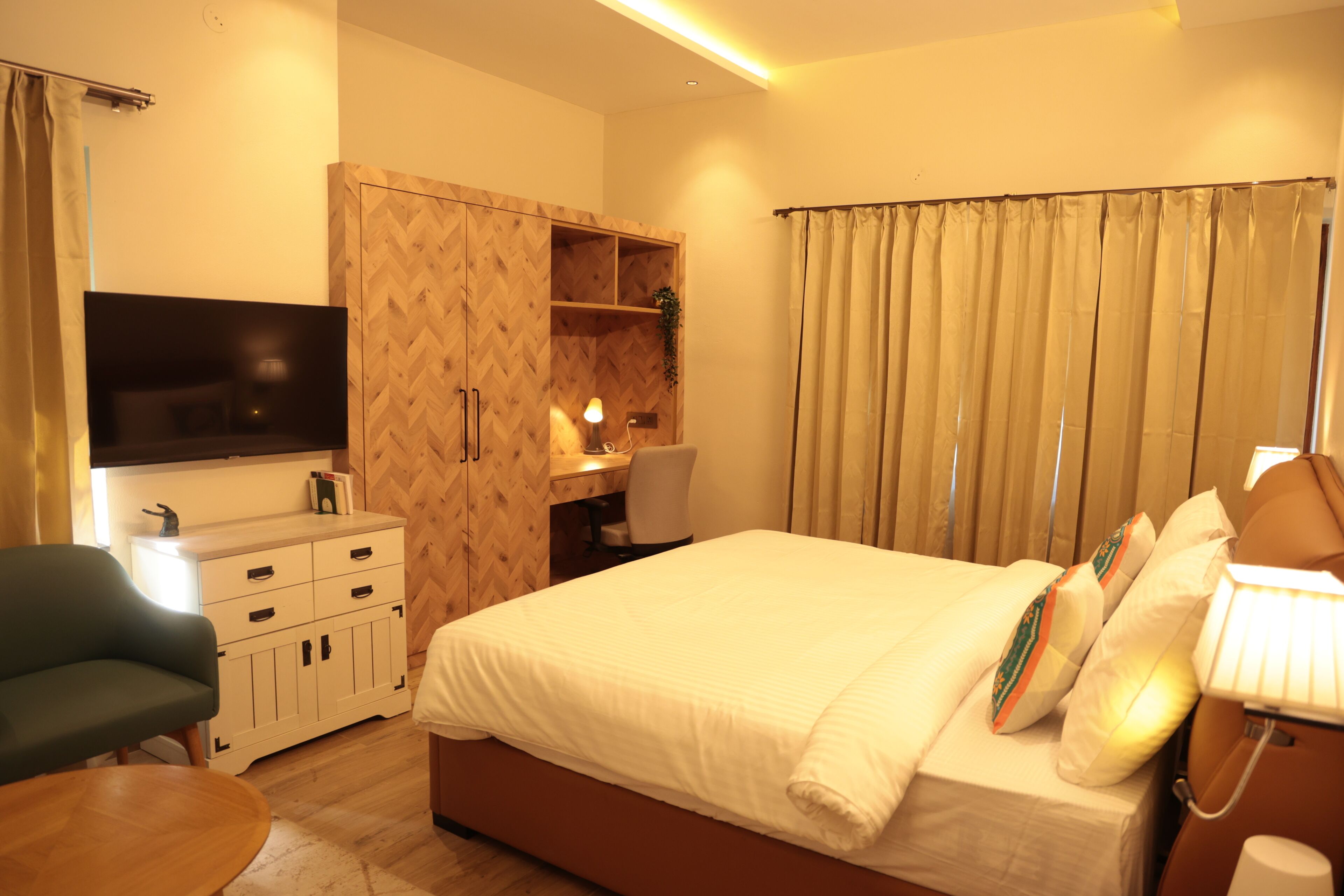A hotel room with a bed, a desk, a chair, a TV, and a wardrobe.