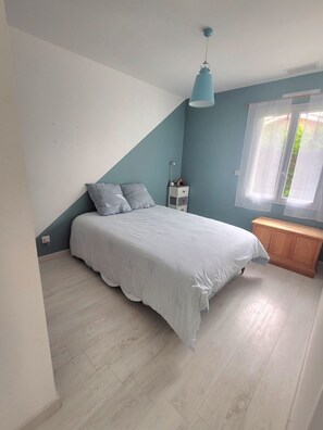 Ein Schlafzimmer mit einem Bett, einem Nachttisch, einer Lampe und einem Fenster.