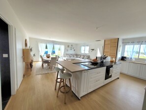 A modern kitchen with a central island, white cabinetry, and a dining area with a table and chairs. - Bright villa with garden and Balnéo 5 min d'Arcachon and 15 min from the beaches (La Teste-de-Buch)