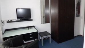Una stanza con un letto, una scrivania, una televisione, un armadio e uno specchio.